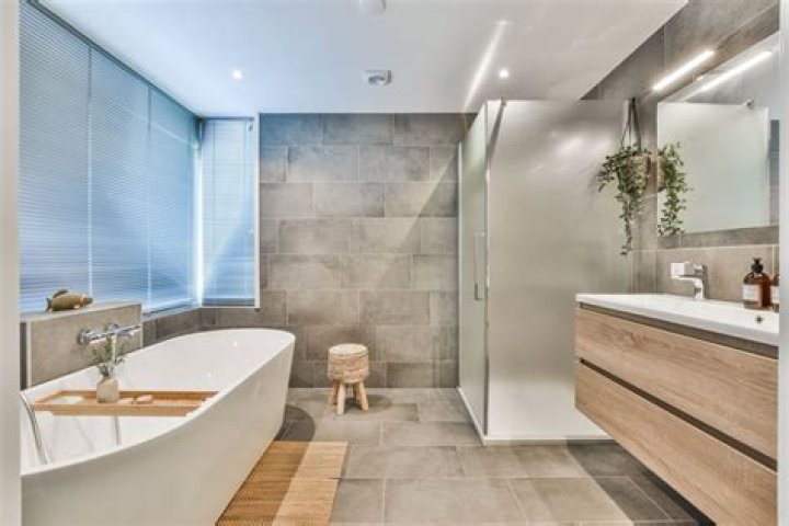 A bathroom at The Ludlow Hotel, featuring a marble bathtub and sink, white-tiled walls, and a window with city views