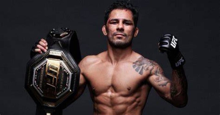 Alexandre Pantoja with flyweight title belt around him in face off with Brandon Royval.