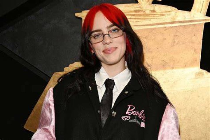 Billie Eilish in a messy bun, skinny glasses, and collared shirt at the Golden Globes