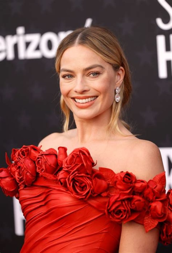 Margot Robbie in a red off the shoulder dress adorned with rosettes.